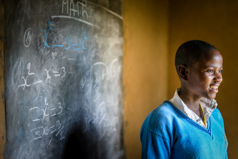 16-year old Isabelle, works on math equations on the blackboard her parents installed at the entrance to the new home they are building in Kisaro, Rwanda. Photography credit: Jon Warren